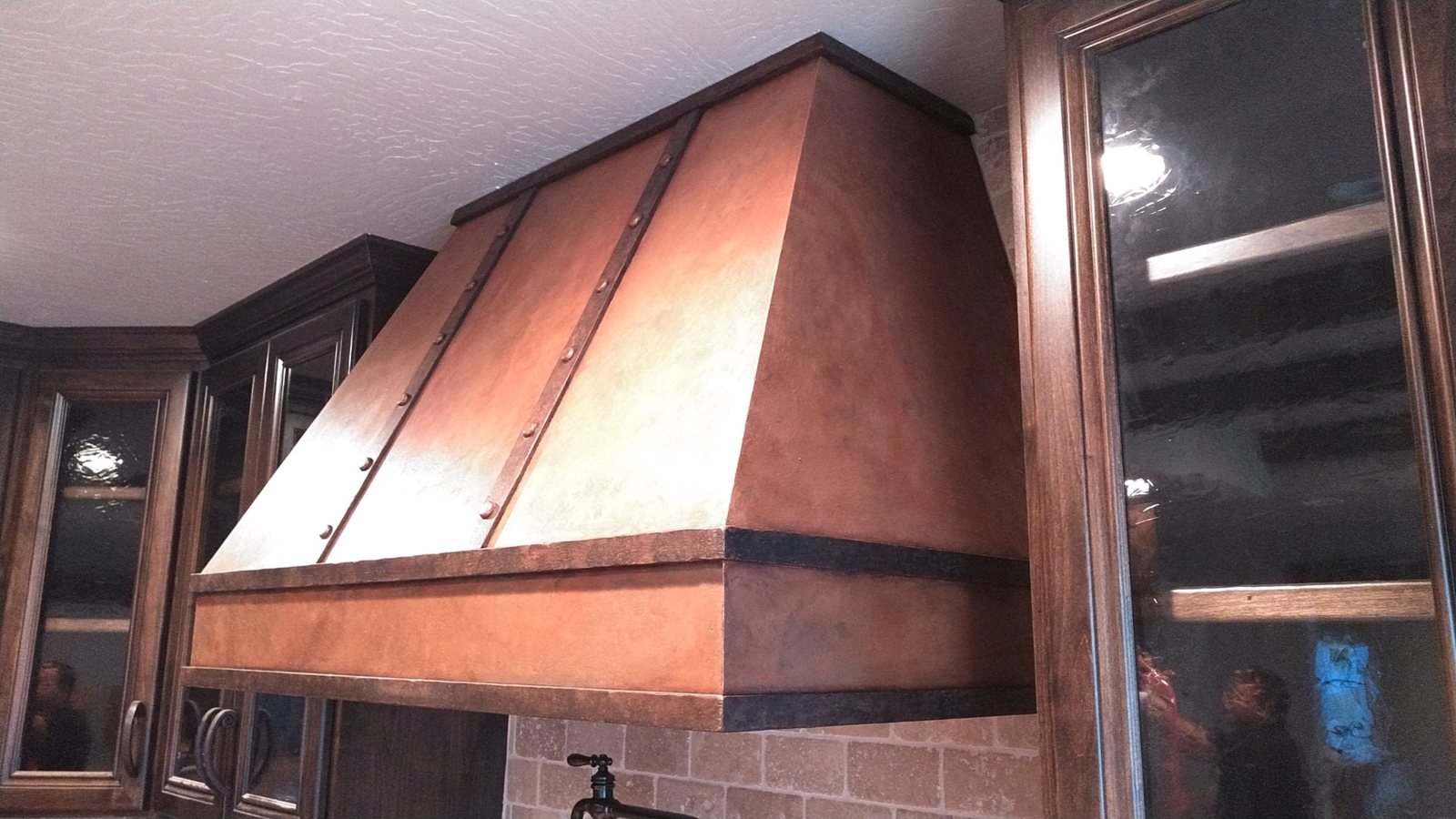 Custom Copper Range Hood — Dark Stained Glass-Front Cabinetry